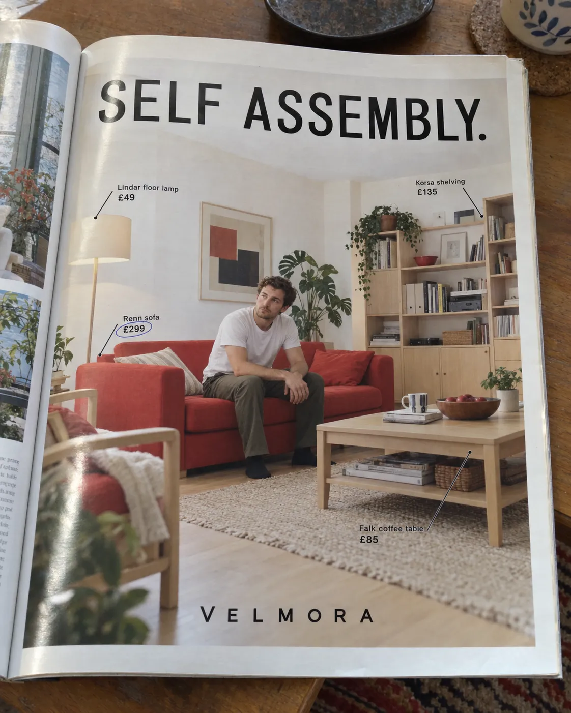 A photograph of an open magazine on a wooden table: a full-page furniture advertisement showing a young man sitting alone on a red sofa in a tidy living room with price labels on the lamp, shelving, sofa and coffee table, under the headline SELF ASSEMBLY. and the invented brand name Velmora. The image is machine-generated; the magazine and the advertisement never existed.